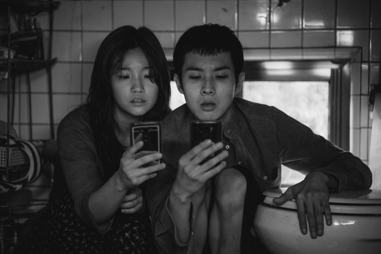 Eine junge Frau und ein Hunger Mann knien nebeneinander und schauen beide in ihre Handys. Das Foto ist schwarz-weiß.
