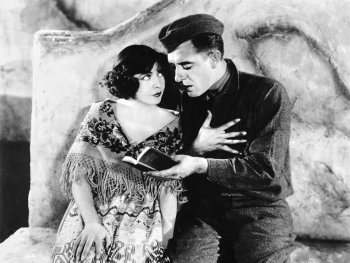 Schwarzweiß-Foto. Ein Soldat liest einer Frau aus einem Buch vor.
