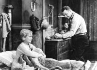 Schwarzweiß-Foto. Ein Junge sitzt in einem Bett. Ein Mann daneben spielt Schattenboxen mit ihm.