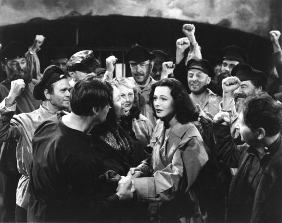 Schwarzweiß-Foto. In der Mitte einer Menschenmenge geben sich eine Frau und ein Mann die Hand.