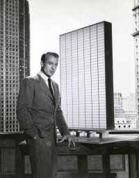 Schwarzweiß-Foto. Ein Mann steht an einem Schreibtisch.