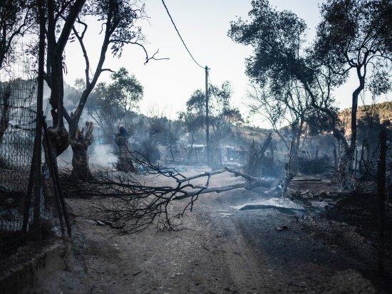 Im Vordergrund sieht man verbrannte Bäume, im Hintergrund die durch das Feuer am 9.9.2020 verwüstete Flüchtlingsunterkunft Moria auf der griechischen Insel Lesbos.