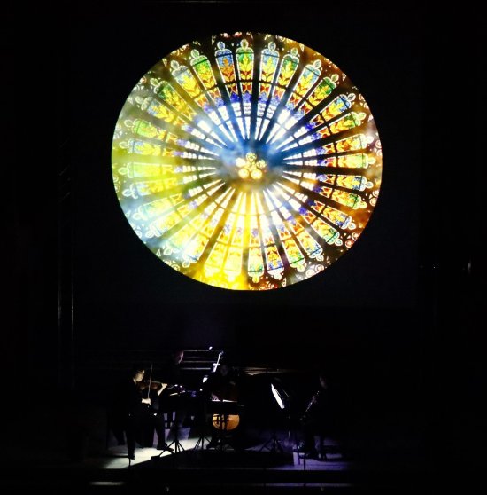 Jessica Hartlieb mit Violine unterhalb eines riesigen, bunten leuchtenden runden Kirchenfensters
