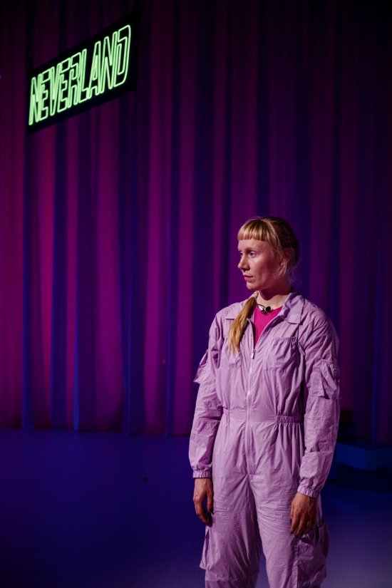 Salome Kehlenbach steht in rosafarbenem Jumpsuit vor dunklem Hintergrund. Über ihr ist "Neverland" in grüner Neonschrift zu lesen.