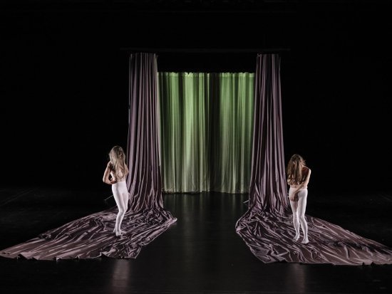 Zwei Tänzerinnen mit langen Haaren stehen rechts und links auf fliederfarbenen langen Vorhang