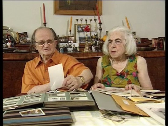 Ein Farb-Foto von Ilse und Kurt Aufochs wie sie an einem Tisch sitzen und Fotoalben anschauen