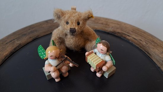 Sitzender Teddybär, davor zwei Figuren mit einem Akkordeon und einer Violine