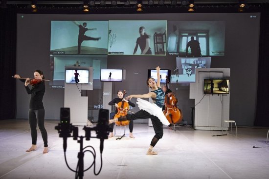 Streichtrio und Ballettänzerin in hellem Bühnenraum, im Hintergrund Projektionen von tanzenden Personen