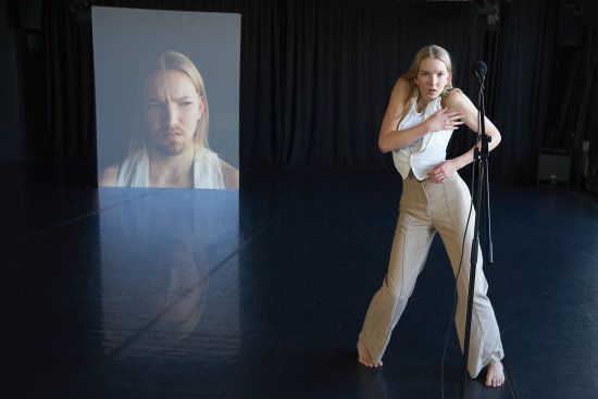 Frau macht eine Pose auf einer schwarzen Bühne, im Hintergrund wird ein Foto projiziert
