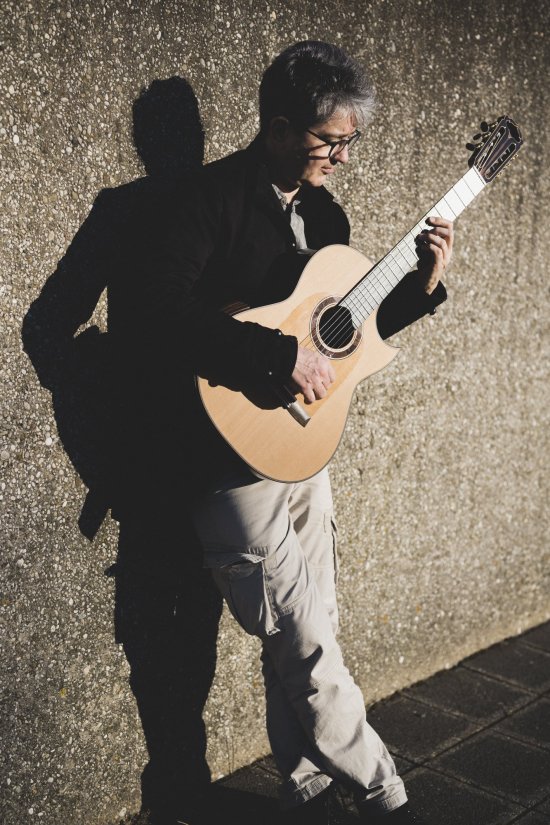 Stefan Grasse lehnt an einer Wand mit einer Gitarren in der Hand