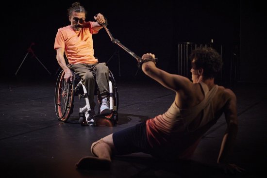 Ein Mann im Rollstuhl und ein Mann, der am Boden liegt strecken sich jeweils eine Krücke entgegen.