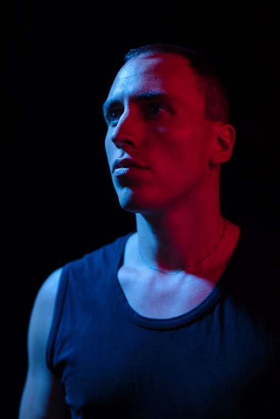 Martin Kohlstedt steht im Unterhemd vor einer schwarzen Wand und wird von rotem Licht beschien.