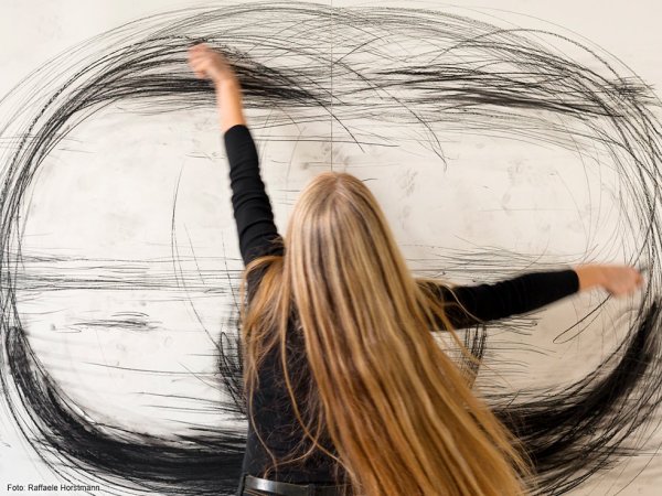 Eine Frau zeichnet mit großen Armbewegungen Kreise auf eine Wand.