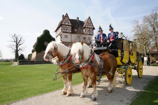 Gelbe Postkutsche mit zwei Pferden und zwei Kutschern vor Schloss Neunhof