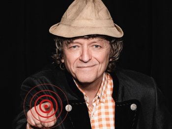 Mann mit hellbraunem Hut, lächelnd zeigt mit dem rechten Zeigefinger auf den Betrachter
