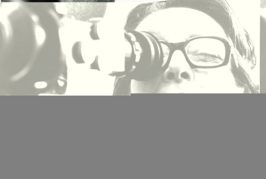 Porträt von Marguerite Duras, die mit einem Auge in eine Filmkamera schaut
