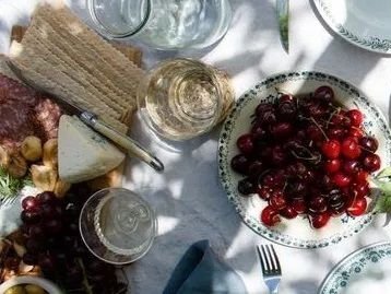 Auf der Abbildung ist eine schön gedeckte Tafel mit Gläsern, Besteck, Früchten, Käse, Salami, Brot zu sehen.