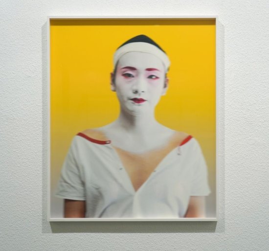 Foto von Eitaro Matsunoyo zum Teil bereits geschminkt für seinen Auftritt als Geisha vor gelbem Hintergrund