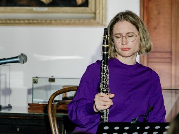 Rebecca Trescher (trägt einen lila Pullover) sitzt vor einem Notenständer und hält ihre Klarinette