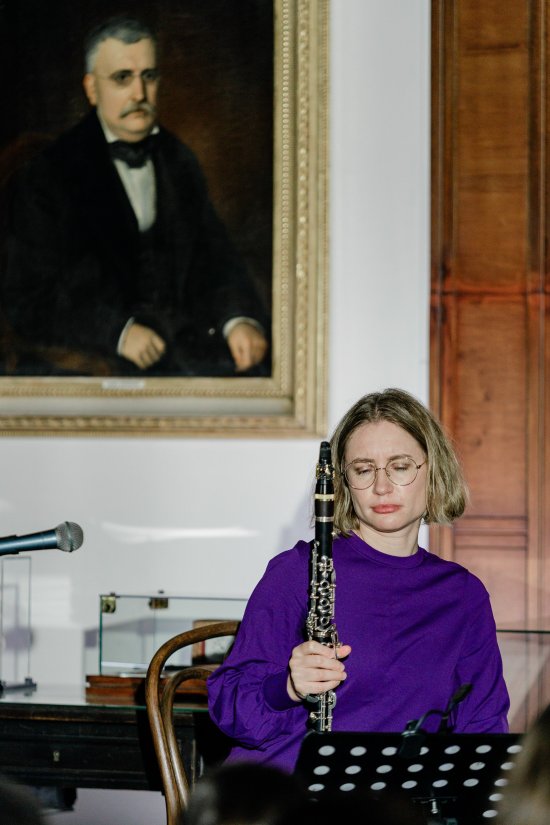 Rebecca Trescher (trägt einen lila Pullover) sitzt vor einem Notenständer und hält ihre Klarinette
