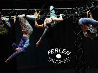 Tänzerinnen hängen an einem Bühnenaufbau, das einem Klettererüst ähnelt