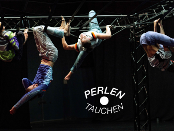 Tänzerinnen hängen an einem Bühnenaufbau, das einem Klettererüst ähnelt