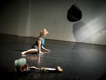 Tänzerin mit einem Bein halbliegend auf dem schwarzen Tanzboden; ihre Prothese liegt nebendran