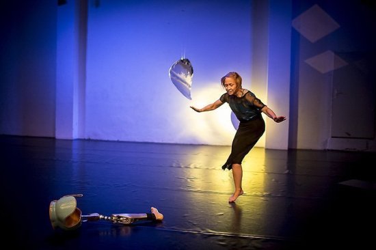 Tänzerin mit einem Bein stehend auf der leicht beleuchteten Bühne, vor ihr liegt die Bein-Prothese