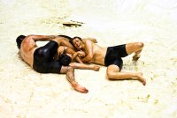 drei Performer*innen (oberkörperfrei und mit einer Schicht Öl bedeckt) wälzen sich auf dem Bühnenboden