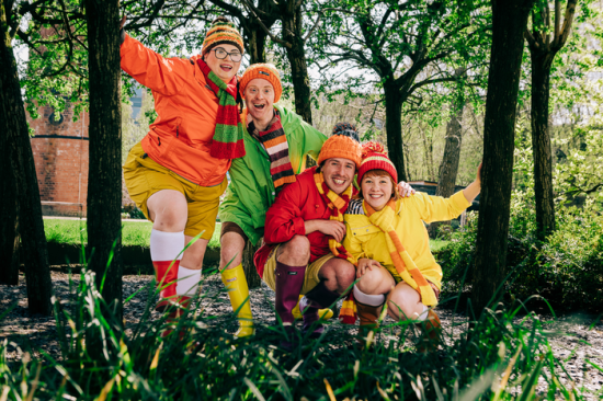 Vier sehr bunt gekleidete lachende junge Menschen mit Pudelmützen im Wald