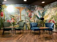 Zwei Sesselpaare (blau und grün) mit je einem Nierentischchen, vor bunt , mit floralen Motiven bemalter Wand