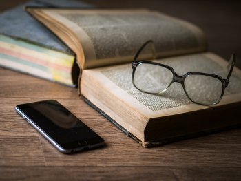 Brille auf Buch daneben ein Smartphone