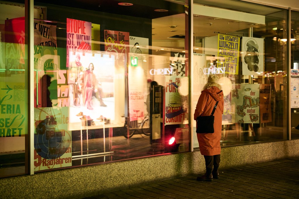 Besucherin der Zukunftsmusik vor Schaufenster mit Plakatausstellung