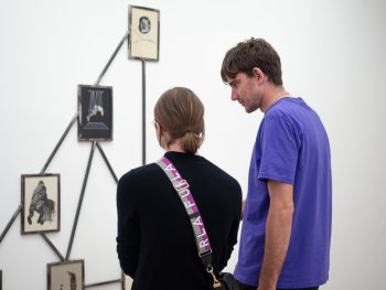 Ein Mann und eine Frau in Seiten- bzw. Rückenansicht, die ein Werk einer Ausstellung betrachten