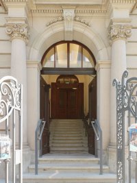 Repräsentativer Eingangsbereich der Kunstvilla mit breitem Rundbogenportal, korinthischen Pilastern, Freitreppe und geöffneten Holztüren.