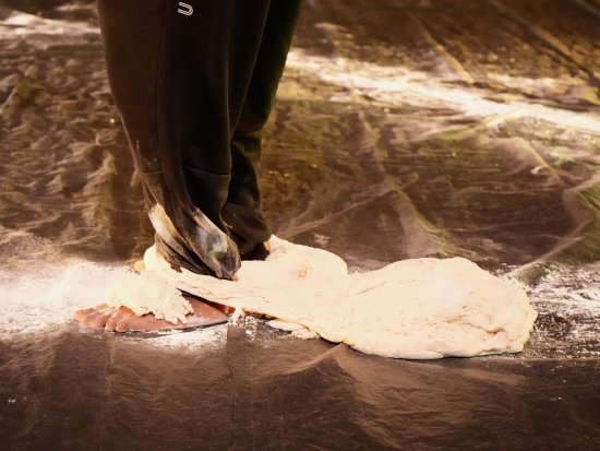 Eine Person, die eine schwarze Jogginghose trägt, steht auf einer schwarzen Plastikplane, um ihre Füße ist eine mehlige Teigmasse gewickelt.