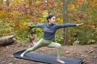 Frau auf Yogamatte im Wald, herbstlich gefärbte Blätter