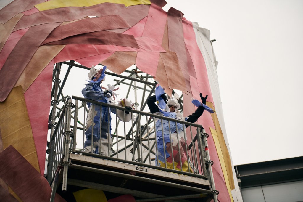 Kostümierte Performer*innen und bekleideter Turm