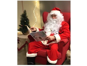 Copyright: Voigt eine als Nikolaus verkleidete Person sitzt in einem roten Sessel vor Weihnachtsdekoration und hält ein aufgeschlagenes Bilderbuch in der Hand