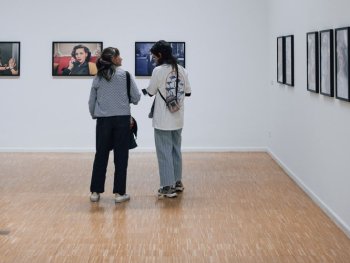 Zwei Personen unterhalten sich in der Ausstellung, im Hintergrund ein Bild von Lauren Becall am Telefon.