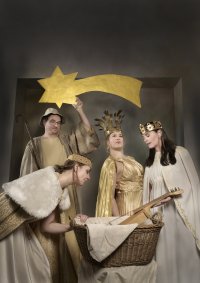 Vier Personen in gold- und cremefarbenen Gewändern, eine hält einen goldenen Stern mit Schweif, eine andere beugt sich über einen Korb mit Tuch und Holzspielzeug.