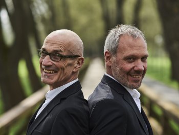 zwei Lächelnde grauhaarige Männer, Rücken an Rücken mit schwarzem Anzug und weißem Hemd