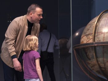 Ein Vater und eine Tochter blicken auf einen Globus hinter einer Vitrine