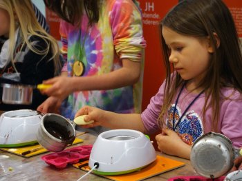 Foto eines jungen Kindes, das geschmolzene Schokolade in Pralinenförmchen gießt.