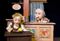 Foto, auf dem der Tischlerlehrling im Wirtshaus Essen auf seinem Tischlein deck dich herbeizaubert und vom gierigen Wirt dabei beobachtet wird.