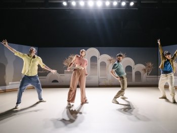 Foto: Sebastian Autenrieth
An der Bühnenkante zwei Männer und zwei Frauen in energetischen Posen, im Hintergrund Gegenlicht der Scheinwerfer, auf der Bühnenrückwand pastellfarbiges Fotomotiv (antike Bögen und Palmen)