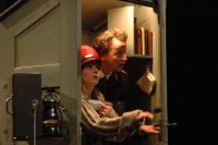 Zwei Personen in einem kleinen, schrankartigen Raum mit Büchern, eine Person öffnet die Tür. Beide schauen erstaunt.