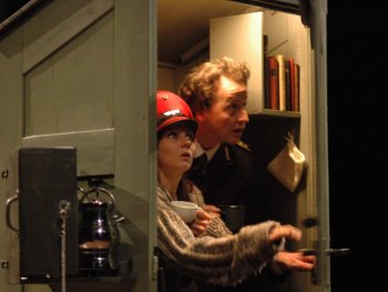 Zwei Personen in einem kleinen, schrankartigen Raum mit Büchern, eine Person öffnet die Tür. Beide schauen erstaunt.