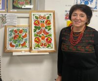 Die Künstlerin Tetiana Liudvychenko steht neben zwei Ihrer gerahmten Kunstwerke