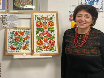 Copyright: Tetiana Liudvychenko Die Künstlerin Tetiana Liudvychenko steht neben zwei Ihrer gerahmten Kunstwerke